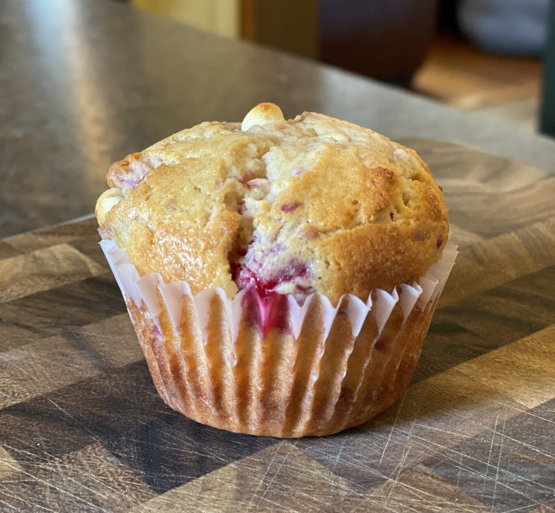 baked raspberry white chocolate chip muffin on wooden cutting board